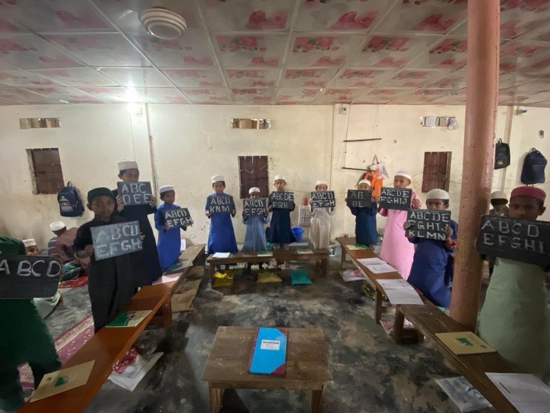 Young madrasah pupils holding chalk slates showing the English alphabet